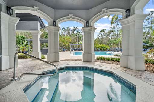 A pool surrounded by white columns and a white roof at The Grand Reserve at Tampa Palms Apartments, Florida