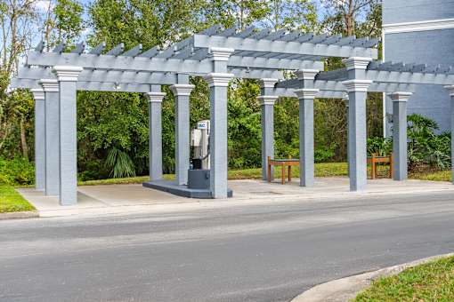 A grey pergola with columns and benches is situated on a paved car wash area at The Grand Reserve at Tampa Palms Apartments, Florida