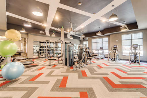 a gym with a variety of exercise equipment and a large window at Dartmoor Place at Oxford Square Apartments, Hanover, MD