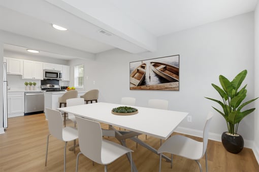 a dining room with a white table and chairs and a white kitchen with stainless steel appliances Kenilworth at Perring Park Apartments, Parkville, MD 21234