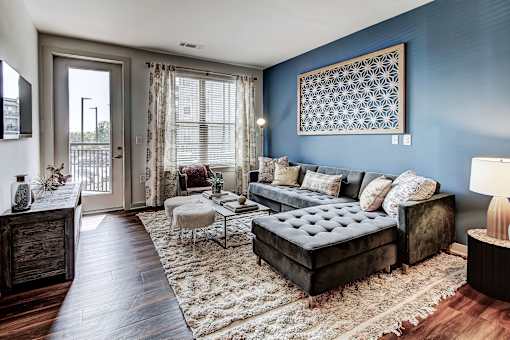 A living room with a dark brown sofa and a tufted ottoman at The Linden Apartments, Davidson, NC