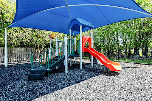 A playground with a blue umbrella and a red slide at Waterview at Coconut Creek, Coconut Creek, FL