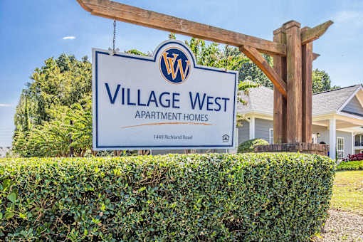 A sign for Village West Apartment Homes stands in front of a building.