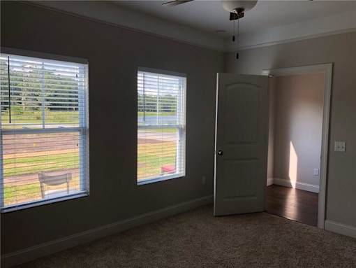 A room with a carpeted floor, a ceiling fan, and a door leading to a backyard.