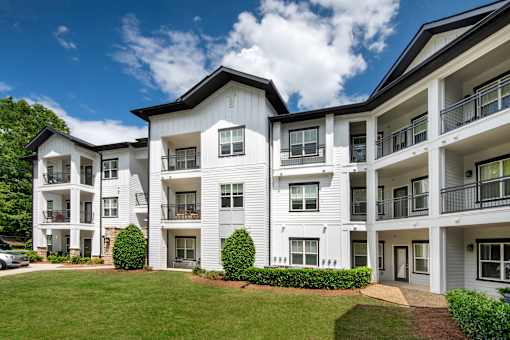 A white apartment building with balconies and a green lawn in front.