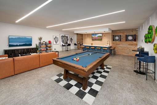 A pool table is in the middle of a room with a bar and a television.