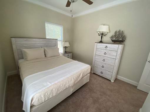 A bedroom with a bed, dresser, and ceiling fan.