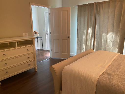 A bedroom with a bed, dresser, and window with curtains.