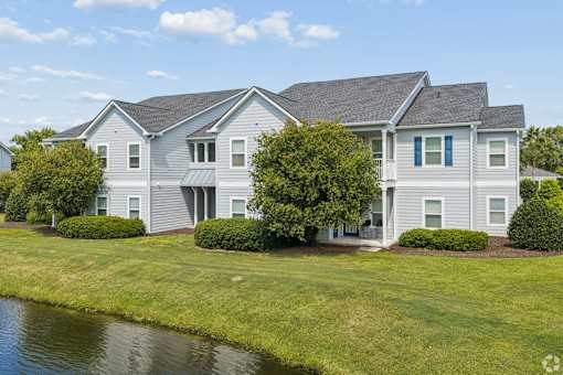 A house with a grey roof and white walls is surrounded by greenery.