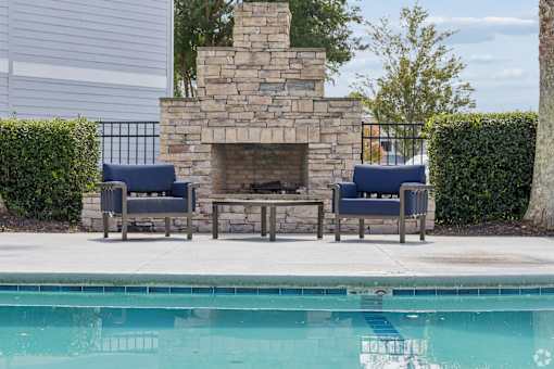 A pool with a stone fireplace and two chairs.