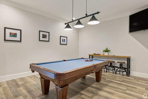 A pool table in a room with a bar stool and a TV.