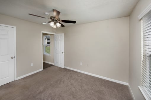 an empty living room with a ceiling fan and window