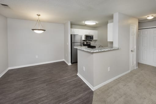 an empty living room and kitchen with a counter top and a refrigerator