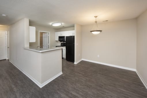 an empty living room with a kitchen and a dark wood floor