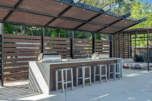 A wooden bar with a concrete counter and stools under a roof.