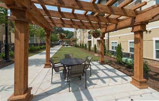 A wooden pergola with a table and chairs is in the foreground of a patio area.