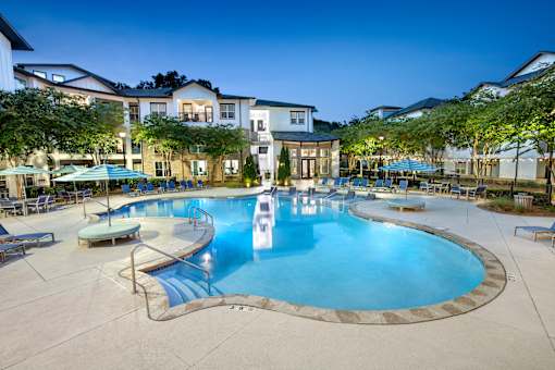 A large swimming pool surrounded by lounge chairs and umbrellas at a resort.