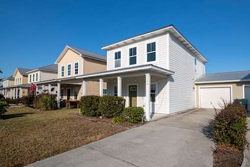 A white house with a grey garage door is in front of a row of houses.