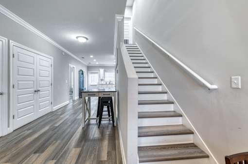 A staircase with a wooden handrail and steps leading to a dining area with a table and chairs.