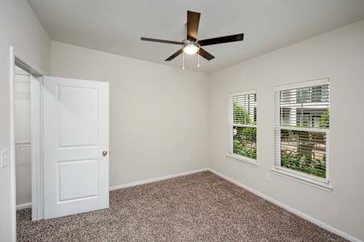 A room with a ceiling fan and two windows.