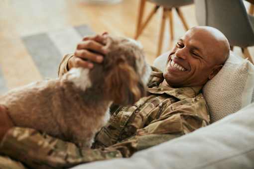 A man in military uniform is laughing while holding a dog.