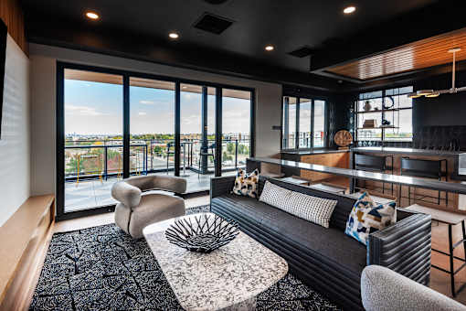 A black couch with a white pillow is in the middle of a room with a large window.