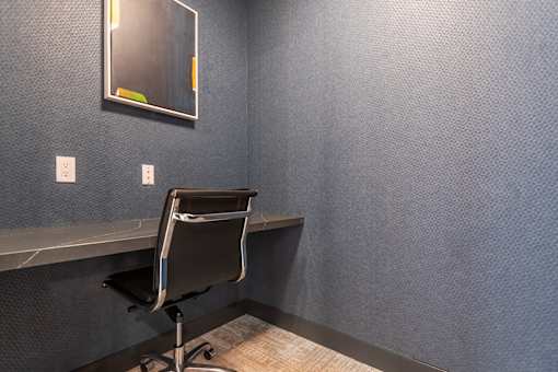 A black chair is in front of a wall with a mirror and two switches.