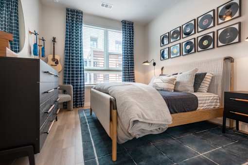 A bedroom with a bed, a chair, a dresser, and a window with curtains.