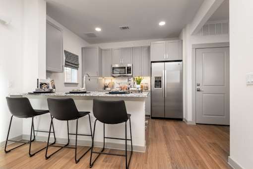 A modern kitchen with a white countertop and black barstools.