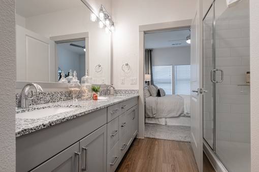 A bathroom with a sink, mirror, and a bedroom in the background.