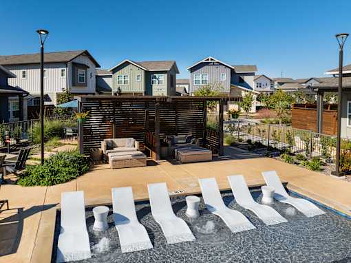 A pool with white chairs and a waterfall in the middle.