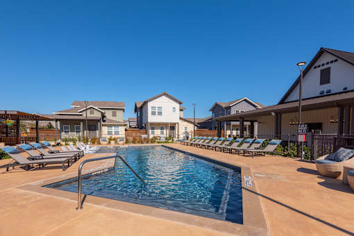 A swimming pool surrounded by lounge chairs in a residential area.