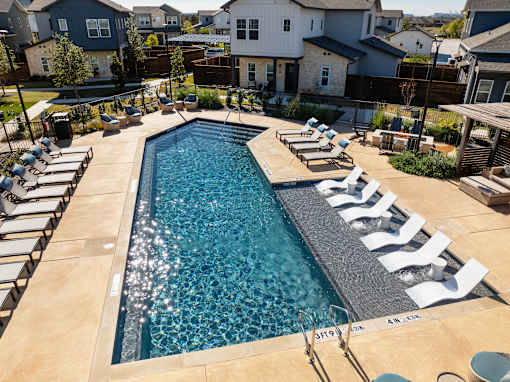 A swimming pool surrounded by a concrete patio and white lounge chairs.