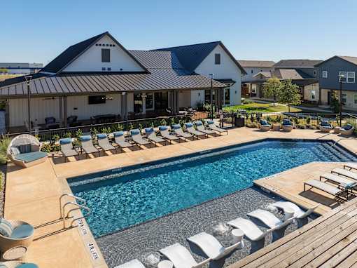 A pool with a wooden deck and lounge chairs in front of a house.