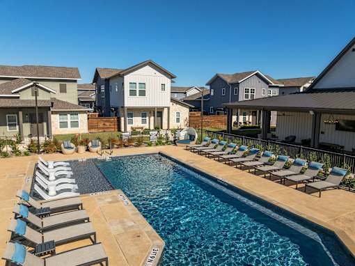 A swimming pool surrounded by lounge chairs in front of a row of houses.