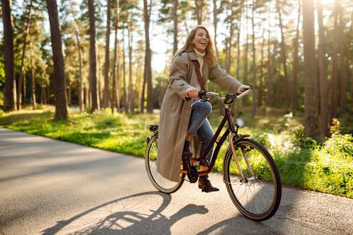 A woman is riding a bicycle on a paved path in a wooded area.