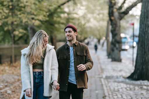 A couple walking hand in hand down a tree-lined street.