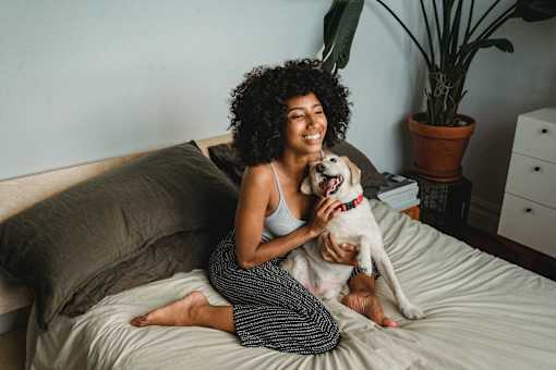 A woman with curly hair is sitting on a bed with a dog.