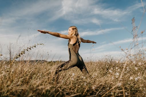 A woman in a black dress is standing in a field with her arms outstretched.