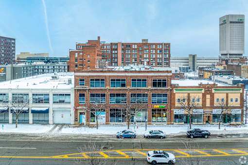 A large building with a red brick facade is in the foreground with cars parked in front.