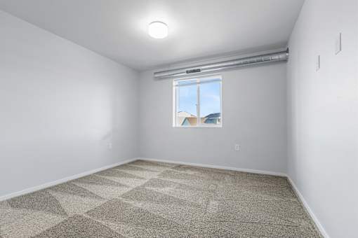 A room with a carpeted floor and a window showing a view of a house.