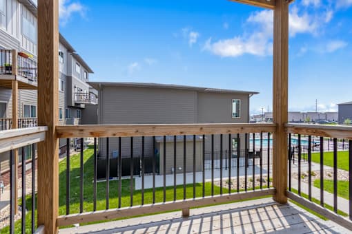 A balcony with a wooden railing overlooks a grassy area and a building.