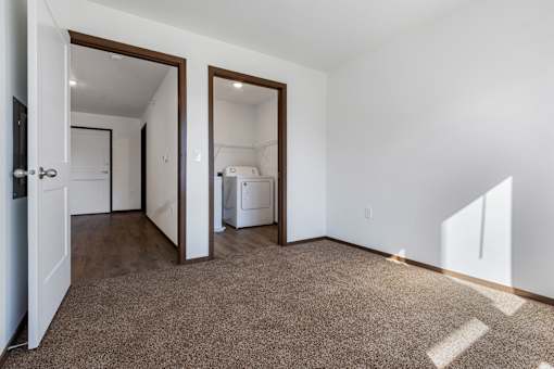 A room with brown carpet and white walls with a doorway leading to another room.