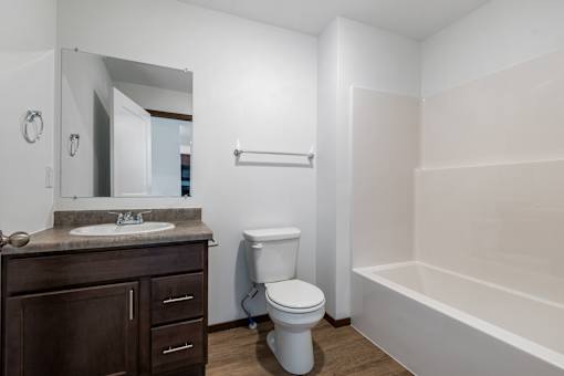 A white toilet sits in a bathroom next to a sink and a bathtub.