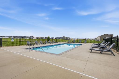 A pool surrounded by a black fence with sun loungers on the side.