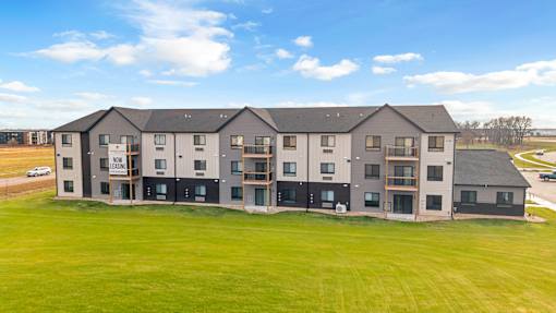 A large building with multiple windows and doors is surrounded by a grassy field.