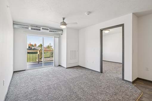 A room with a grey carpet and a sliding glass door leading to a balcony.