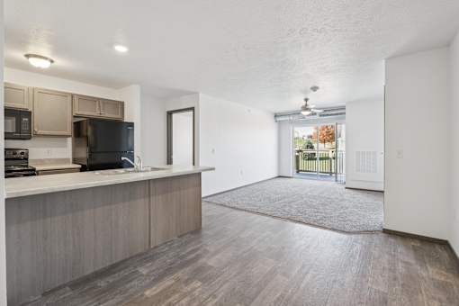 A kitchen with a black fridge and microwave, a wooden floor, and a door leading to a balcony.
