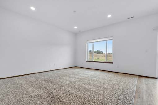A large empty room with a carpeted floor and a window.