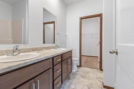 A bathroom with a sink, mirror, toilet and a door.